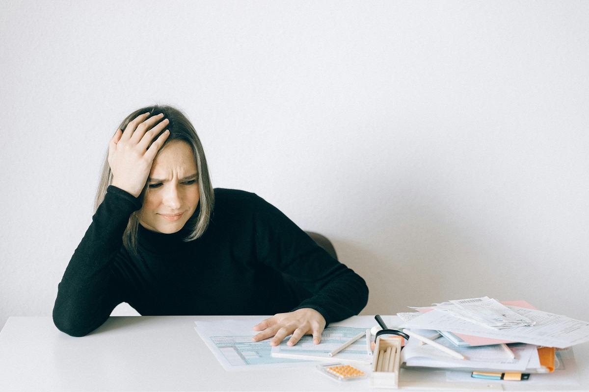 stressed woman in a black sweater sitting at a desk full of financial documents